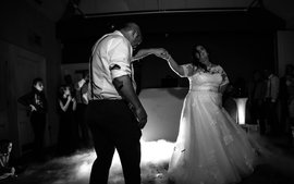 newly wed couple doing first dance in black white with guests and wedding dj in background